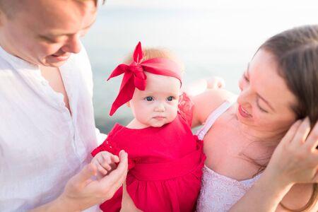 Beautiful family portrait near the sea. Happy parents are holding a little daughter.の写真素材