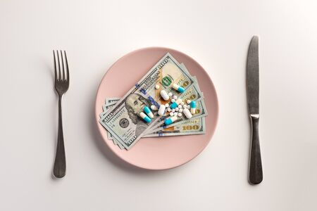 Pills and money on the plate with fork and knife isolated on white backgroundの写真素材