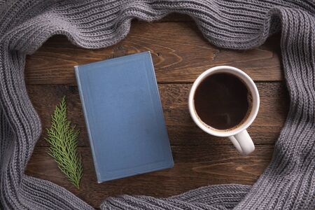 Winter, cozy composition. Warm scarf, book and cup of coffee, on wooden background. Flat lay, top view, copy space.の写真素材
