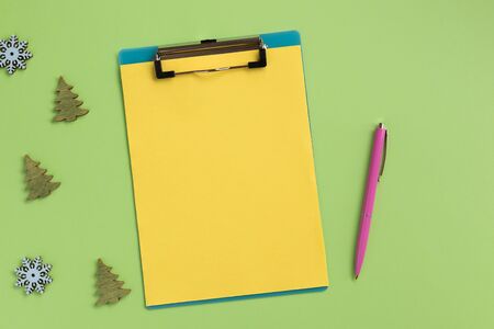 Clipboard with yellow sheet and christmas decor, on green background. Flat lay, top view, copy space.の写真素材