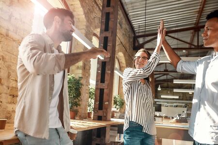 Give me five! Young man and woman giving high-five while having coffee break with colleagues in the modern officeの写真素材