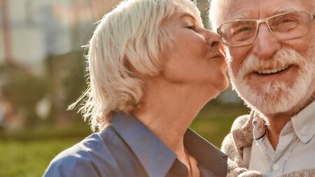 Beautiful senior woman kissing her husband on the cheek while standing in the park together. Family. Love conceptの写真素材