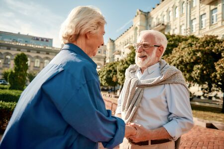 You are making me happy! Beautiful elderly couple holding hands and looking at each other with smile while standing outdoorsの写真素材
