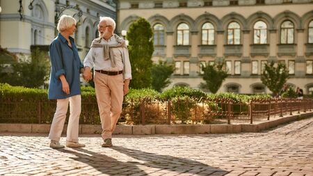 Romantic day. Beautiful and happy elderly couple holding hands and talking about something while walking through the park togetherの写真素材