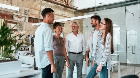 Happy and successful. Group of cheerful business people standing in the modern office, smiling and discussing somethingの写真素材