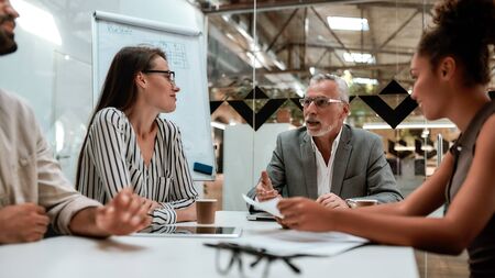 Morning meeting. Group of business people discussing something and smiling while sitting at the office table together. Brainstorming. Teamworkの写真素材