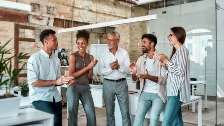 Congratulations! Happy business people clapping their hands and smiling while standing in the creative office. Celebrating successの写真素材