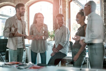 Group of cheerful business people discussing something and smiling while standing in the modern office. Team. Office lifeの写真素材