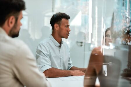 At the meeting. Young african man discussing something with his colleagues while sitting at the office tableの写真素材