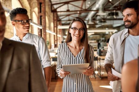 Business professionals. Young and cheerful african woman holding laptop and looking at camera with smile while standing with her colleagues in the modern office. Meetingの写真素材