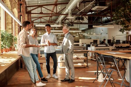 Fast meeting. Business people holding coffee cups and talking about something while standing in the modern office. Coffee break. Teamworkの写真素材