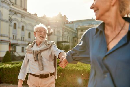 Come with me. Beautiful and happy elderly couple holding hands and smiling while spending time together outdoors on a sunny day. Family. Love concept. Happy momentsの写真素材