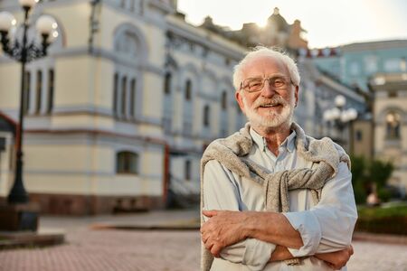 Always in good mood. Portrait of handsome bearded senior man in glasses looking at camera and smiling while standing outdoors. Old age. Happinessの写真素材