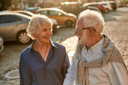 Portrait of happy elderly couple holding hands and looking to each other with smile while walking together through the street. Family. Love conceptの写真素材