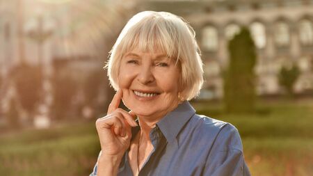 Portrait of happy and beautiful senior woman looking at camera and smiling while standing outdoors on a sunny day. Old age. Happinessの写真素材