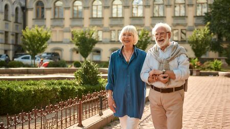 Perfect weather! Happy and beautiful elderly couple holding hands while walking together outdoors. Family. Love conceptの写真素材