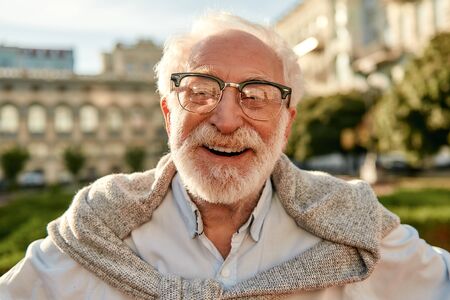 Feeling so happy! Portrait of handsome bearded senior man in glasses looking at camera and smiling while standing outdoors on a sunny day. Old age. Happinessの写真素材