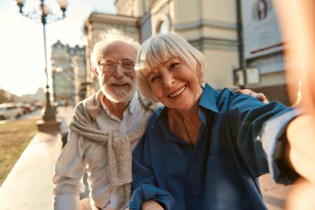 Happy moments together. Cheerful senior couple in casual clothes making a selfie while sitting on the bench outdoors. Modern technologies. Photo conceptの写真素材