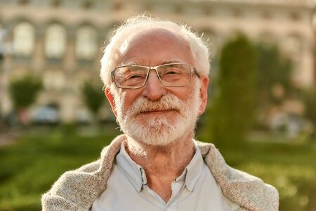 Positive attitude. Portrait of handsome bearded senior man in glasses looking at camera and smiling while spending time outdoors on a sunny day. Old age. Happinessの写真素材