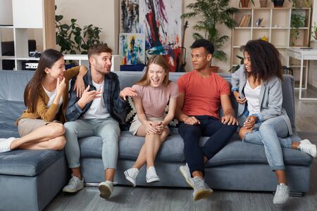 Spending nice time together. Group of young happy multicultural people in casual wear laughing while sitting together on the sofa at home. They relaxing together in the modern apartmentの写真素材
