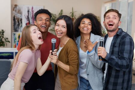 Best friends having fun. Group of young happy multicultural friends singing with microphone together, playing karaoke at home, spending nice time together. Karaoke partyの写真素材