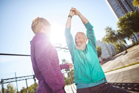 Morning exercises. Happy mature family couple in sportswear warming up together at outdoor gym in the morning, they are doing stretching exercises outdoorsの写真素材