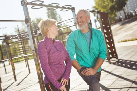 Warming up. Happy mature family couple in sportswear doing gymnastics together at the stadium. Man and woman doing stretching exercises outdoorsの写真素材