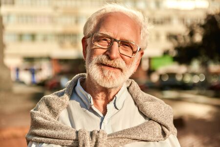 Life is beautiful. Portrait of happy and handsome bearded senior man in glasses looking at camera and smiling while spending time outdoors on a sunny dayの写真素材