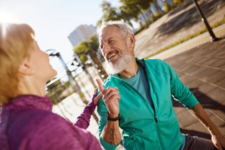 Sporty happy mature man discussing something with his wife while exercising together in the early morning, senior couple doing sport outdoors and talkingの写真素材