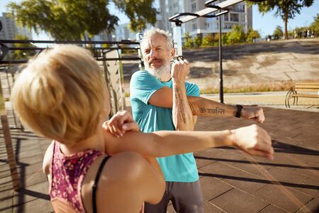Physically active in any age. Athletic mature family couple in sportswear doing stretching exercises in the early morning outdoors, aged couple doing sport togetherの写真素材