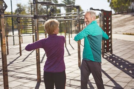 Sport activities in the early morning. Active mature family couple in sportswear exercising, doing sport together while standing at the stadiumの写真素材