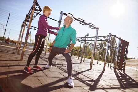 Sporty mature woman talking something to her husband while doing sport together outdoors. Happy mature couple in sportswear exercising together in the early morning at the stadiumの写真素材
