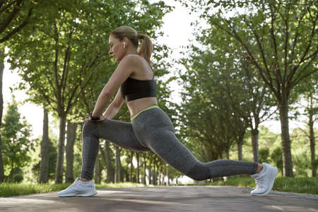 Staying flexible. Full length of beautiful fitness woman in sportswear doing stretching exercises in the city park on a sunny summer morningの写真素材