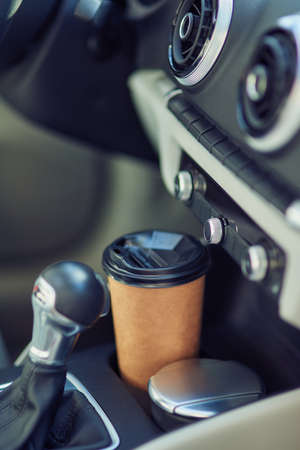 Drinking coffee in car. Vertical shot of a paper cup of coffee in the cup holder between seatsの写真素材