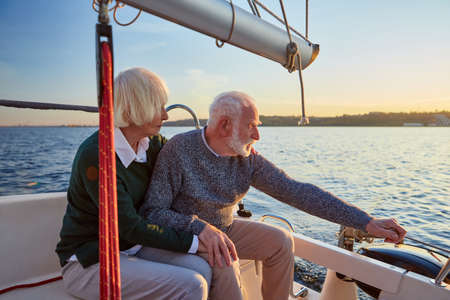 People lifestyle concept. Senior couple, elderly man and woman sitting on the sailboat or yacht deck floating in sea, sailing together on a sunny dayの写真素材