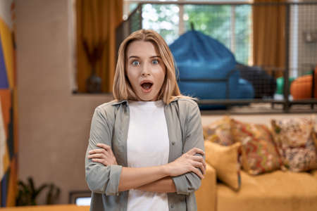 Portrait of a young surprised woman, female office worker keeping mouth opened and looking at camera while standing in the modern officeの写真素材