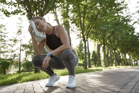 Working hard. Tired fitness woman in sportswear feeling exhausted after active morning workout in the city park. Sport and healthy lifestyleの写真素材