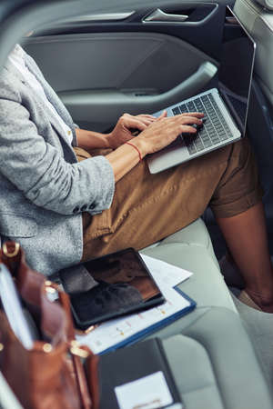 Working online in taxi, vertical shot of business woman using laptop while sitting on back seat in the carの写真素材