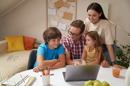 Young happy family working on laptop together, parents helping children with homework or studying online at home during covid 19 quarantineの写真素材