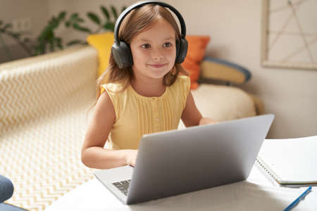 Learning online. Cute and smart little caucasian girl in headphones watching video lesson on laptop...