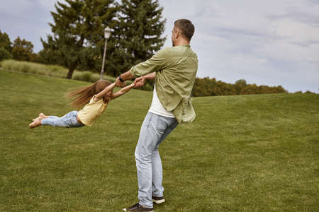 Young loving father playing and having fun with his cute little daughter while visiting beautiful green park on a warm summer dayの写真素材