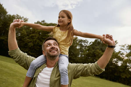 Little excited girl playing with father in park, sitting on his shoulders and smiling, they are spending great time together and having funの写真素材