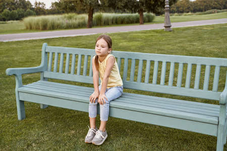 Cute little girl sitting on a wooden bench in park, child spending time outdoorsの写真素材
