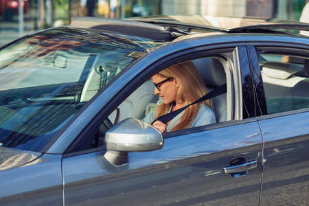 Before you drive away. Beautiful caucasian woman, business lady sitting behind steering wheel of her car and fastening seat beltの写真素材