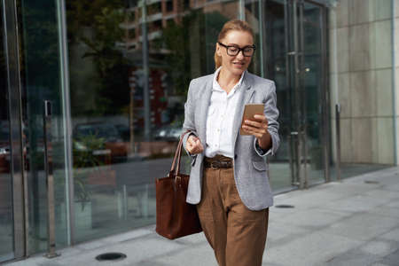 Checking important email. Portrait of a confident attractive business woman in classic wear using smartphone on the way to officeの写真素材