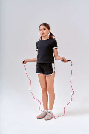Children and sport. Full-length shot of a cute teenage girl skipping with a jump rope isolated over grey background in studioの写真素材