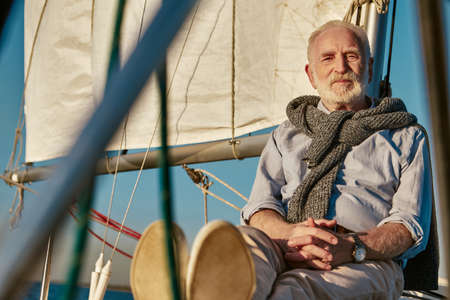 Sailing man. Portrait of a relaxed senior man sitting on the side of his sailboat or yacht deck...