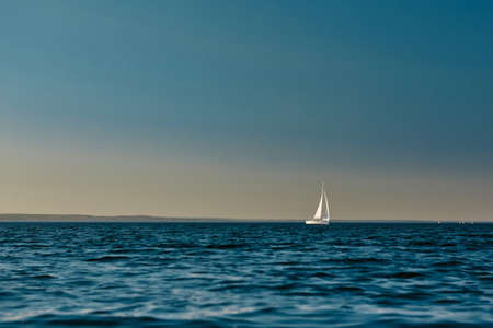Sailing boat or yacht with open white sails floating on the sea at sunset. Majestic landscape, calm...