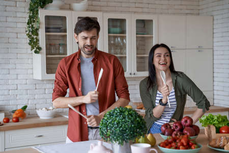 Cooking together. Happy and beautiful young family couple having fun while preparing healthy food in the modern kitchen at home, enjoying free timeの写真素材