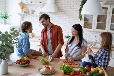 Preparing a salad. Lovely family of four cooking together in the modern kitchen at homeの写真素材